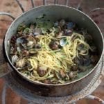 A large metal pot filled with linguine with clams resting on a metal stand