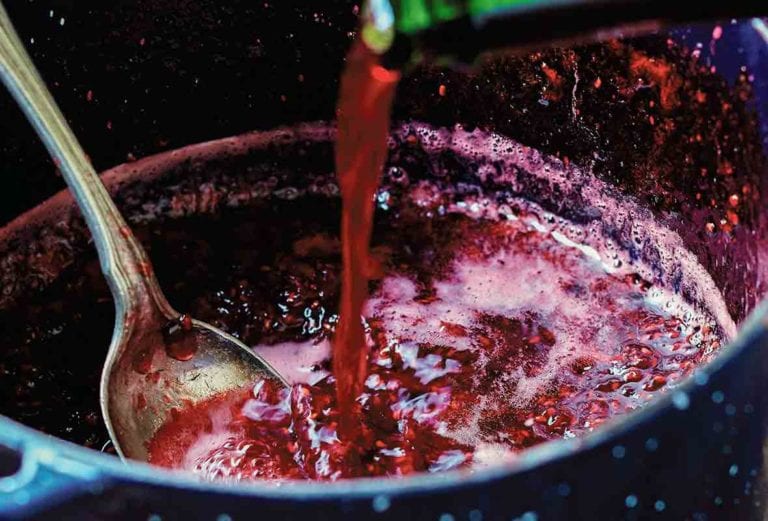 A pot of raspberry jam with framboise being added to it.