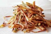A pile of baked french fries, sprinkled with salt and fresh parsley on a paper towel.