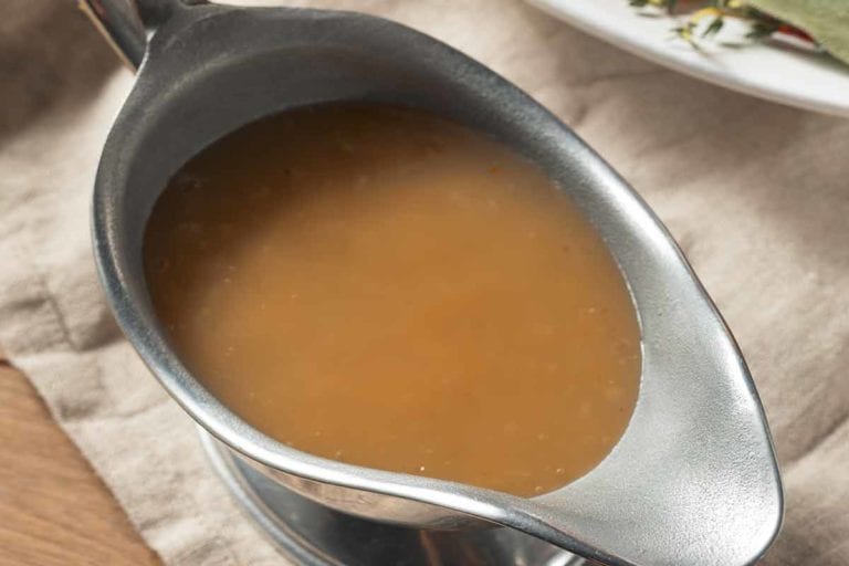 A silver gravy boat filled with gluten-free gravy on a linen cloth.