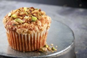 A single apple spice muffin with streusel and pistachios on an inverted metal cake tin.