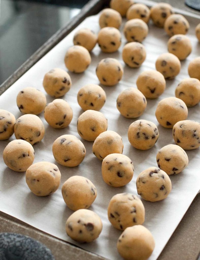 Our guide to freezing food properly--balls of frozen chocolate chip cookie dough on a parchment-lined baking sheet.
