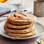 A stack of four gluten-free banana oat pancakes with syrup being poured over the top.
