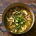 A large blue Dutch oven filled with green chicken chili, topped with sliced jalapenos.