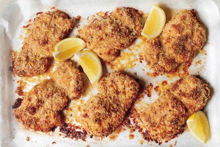 Six breaded oven fried chicken thighs with four lemon wedges in a parchment-lined dish.