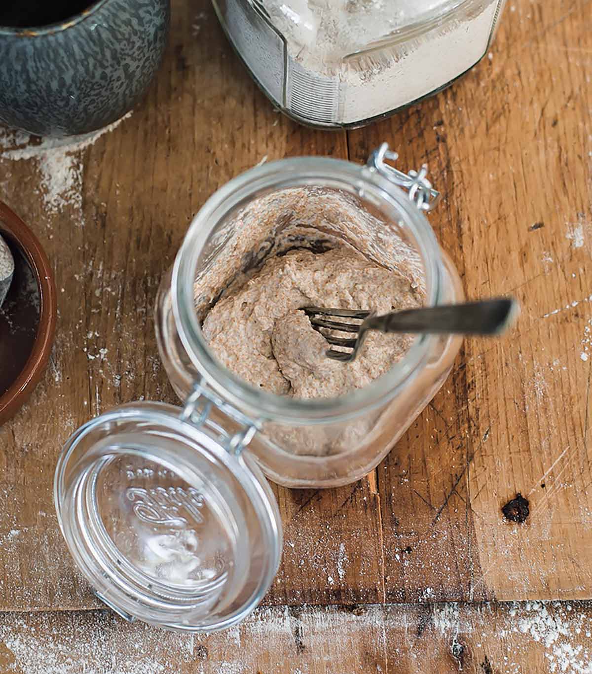 A glass jar with a fork and flour and water as part of an explanation on how to make sourdough starter.