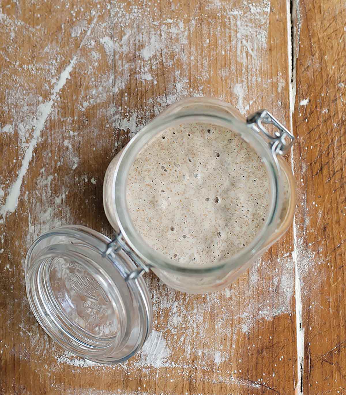 A glass jar with lightly bubbling starter as part of an explanation on how to make sourdough starter.