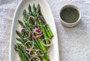 A white oval platter filled with asparagus with raspberry-shallot vinaigrette, and pickled shallots scattered on top.