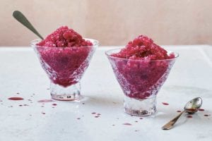 Two small glass dishes of blood orange granita, one with a spoon in it and the other with a spoon resting beside it.