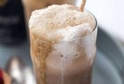 Two Guiness floats with straws on a grey metal try with a few spoons lying beside them.