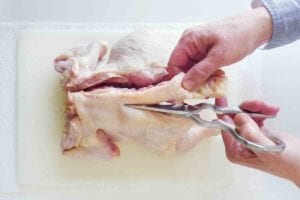 A person cutting through the backbone of a chicken to spatchcock it.