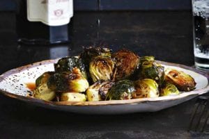 A plate of roasted Brussels sprouts with a drizzle of balsamic vinegar splashing down on it