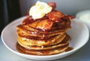 A stack of easy gingerbread pancakes topped with bacon, maple syrup, and creme fraiche in a white bowl.