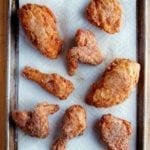 Seven pieces of gluten-free fried chicken on a paper towel-lined rimmed baking sheet.
