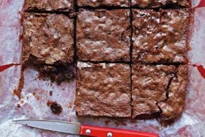 A slab of Katharine Hepburn brownies cut into 9 pieces, on parchment paper, with a knife nearby