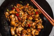 A wok filled with kung pao chicken with two chopsticks on the edge