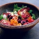 A ceramic bowl filled with mixed green salad with Prosciutto and cherries and drizzled with creamy Dijon dressing.