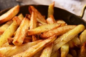 A metal bowl with handles filled with seasoned perfect French fries.
