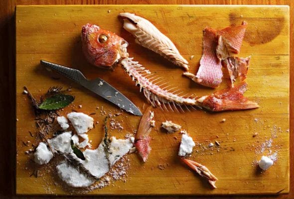 A salt-baked red snapper with all the flesh removed from the bones and a broken salt crust and knife beside the fish skeleton.