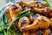 Square plate of a pile of grilled sweet and sticky sriracha drumsticks and grilled scallions