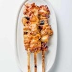 A white oval serving platter topped with three skewers of chicken yakitori with honey sauce.