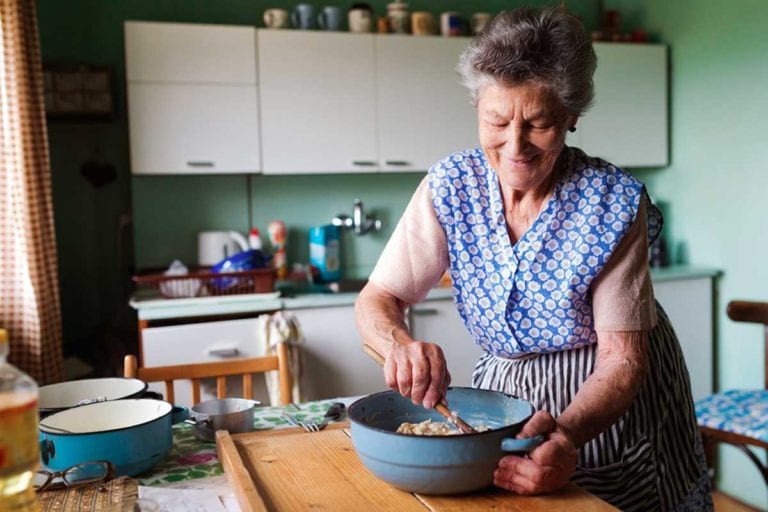 An elderly woman mixing bater in a enameled bowl to illustrate how cooking reminds you who you are.