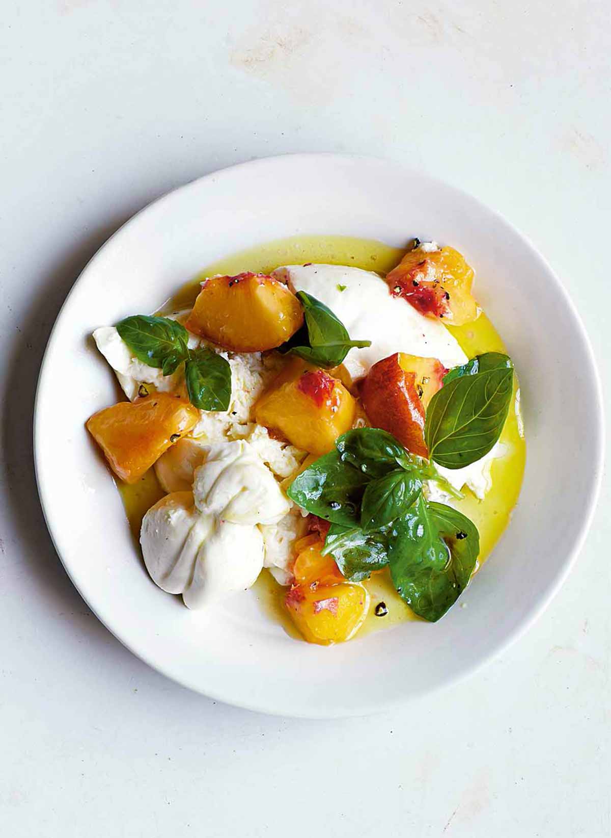 A white bowl filled with peach, burrata, and basil salad.