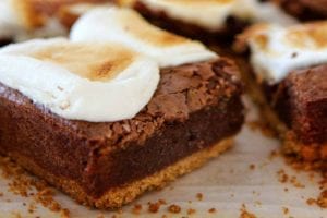 Several bars of cut s'mores brownies made with graham crust, fudgy layer and topped with marshmallow on a piece of parchment.