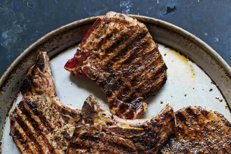 Six coffee-crusted grilled pork chops on a speckled platter.