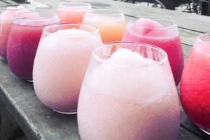 Glasses filled with various flavors of frosé or frozen rosé on a wooden table.