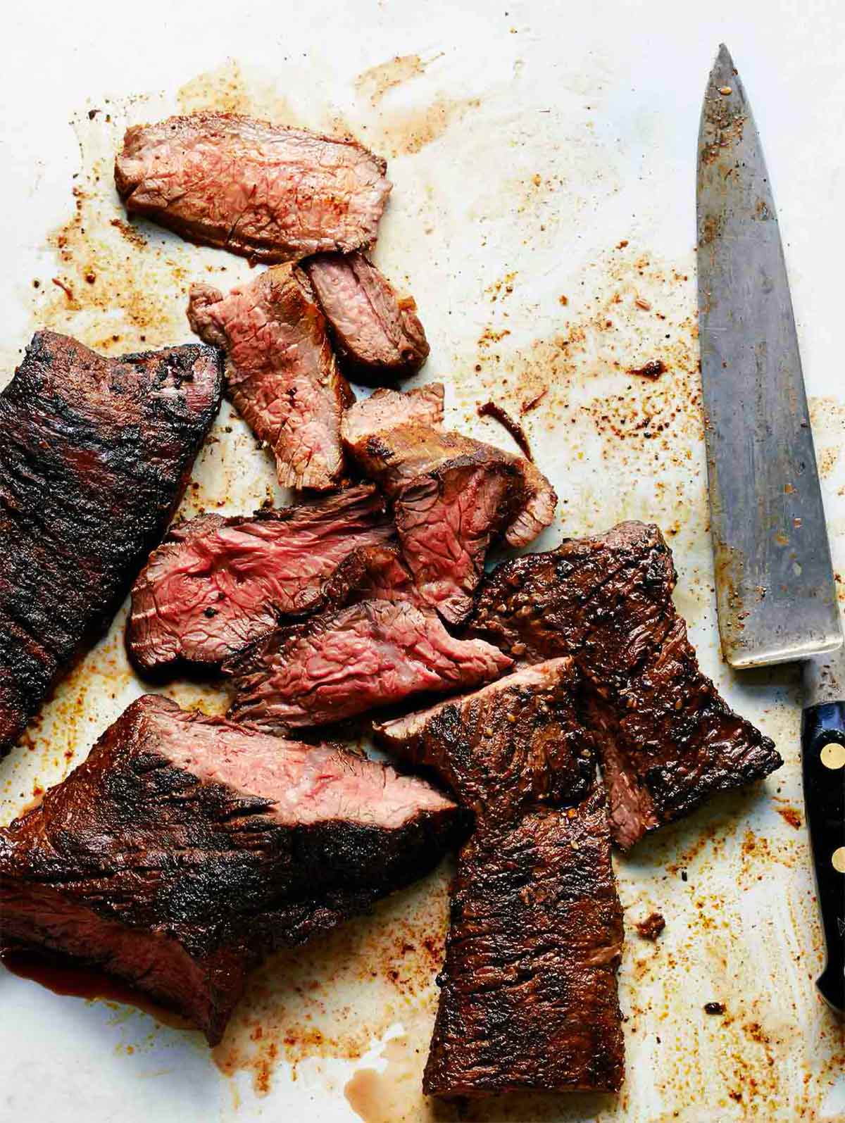 A sliced grilled steak with coffee spice rub and a carving knife lying beside it