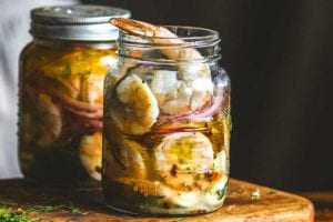 Two jars of pickled shrimp on a wooden cutting board.
