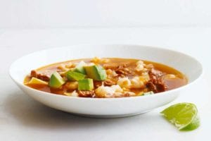 A white bowl filled with quick posole with pork topped with avocado with a lime wedge on the side.