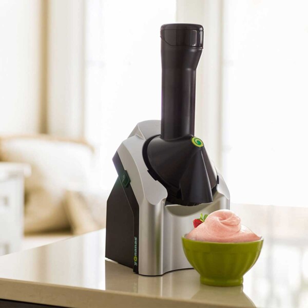 A Yonanas fruit soft serve maker with a bowl of homemade soft serve in a green bowl.