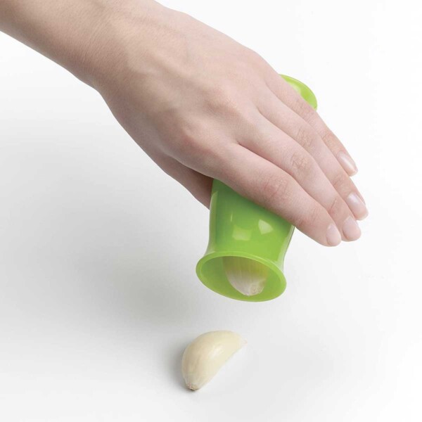 A person shaking peeled cloves of garlic out of a green OXO good grips garlic peeler.