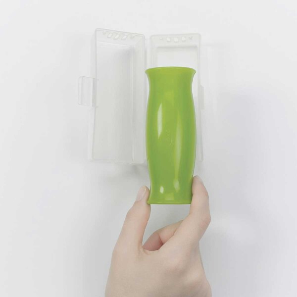 A person placing a green OXO good grips garlic peeler in a clear plastic case.