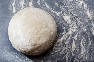 A ball of semolina pizza dough on a floured surface.