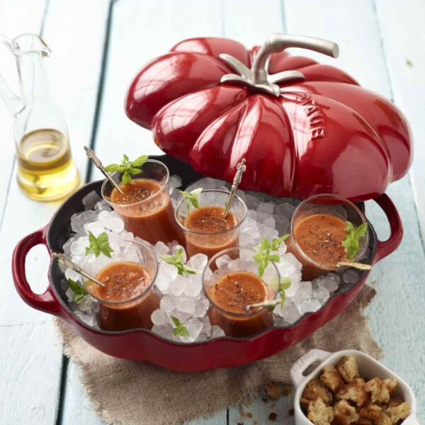 A red Staub Cast Iron 3qt Tomato Cocotte shown open with chilled gazpacho cups on ice.