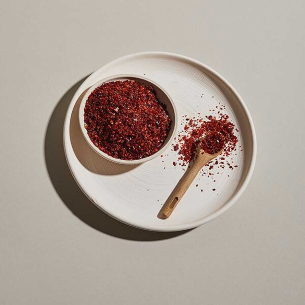 Aleppo Peppers shown with small wooden spoon on white plate.