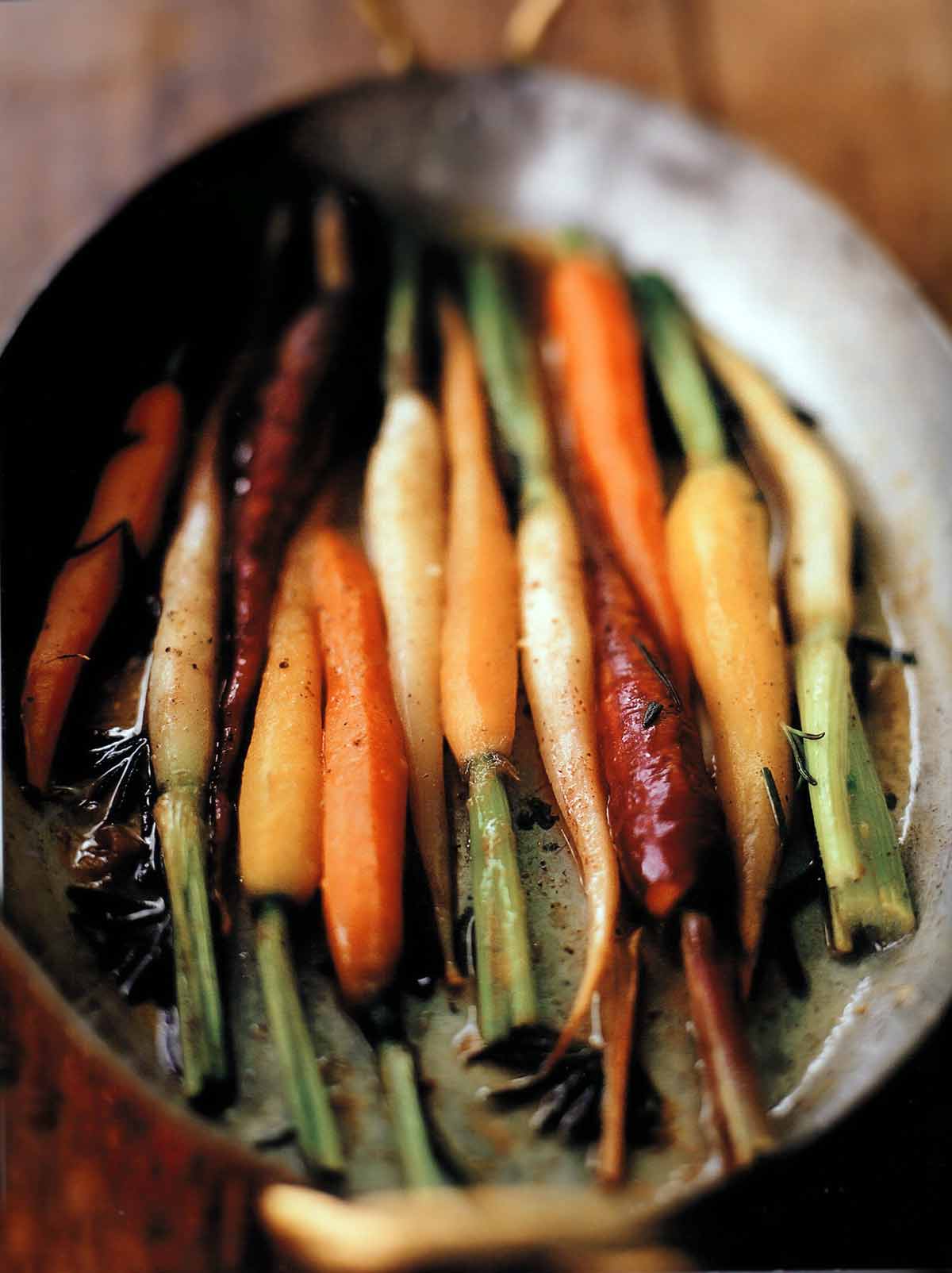 Assorted colors of braised carrots with orange and rosemary in a dish.