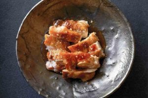 Pieces of sliced chicken with teriyaki sauce in a pewter bowl.