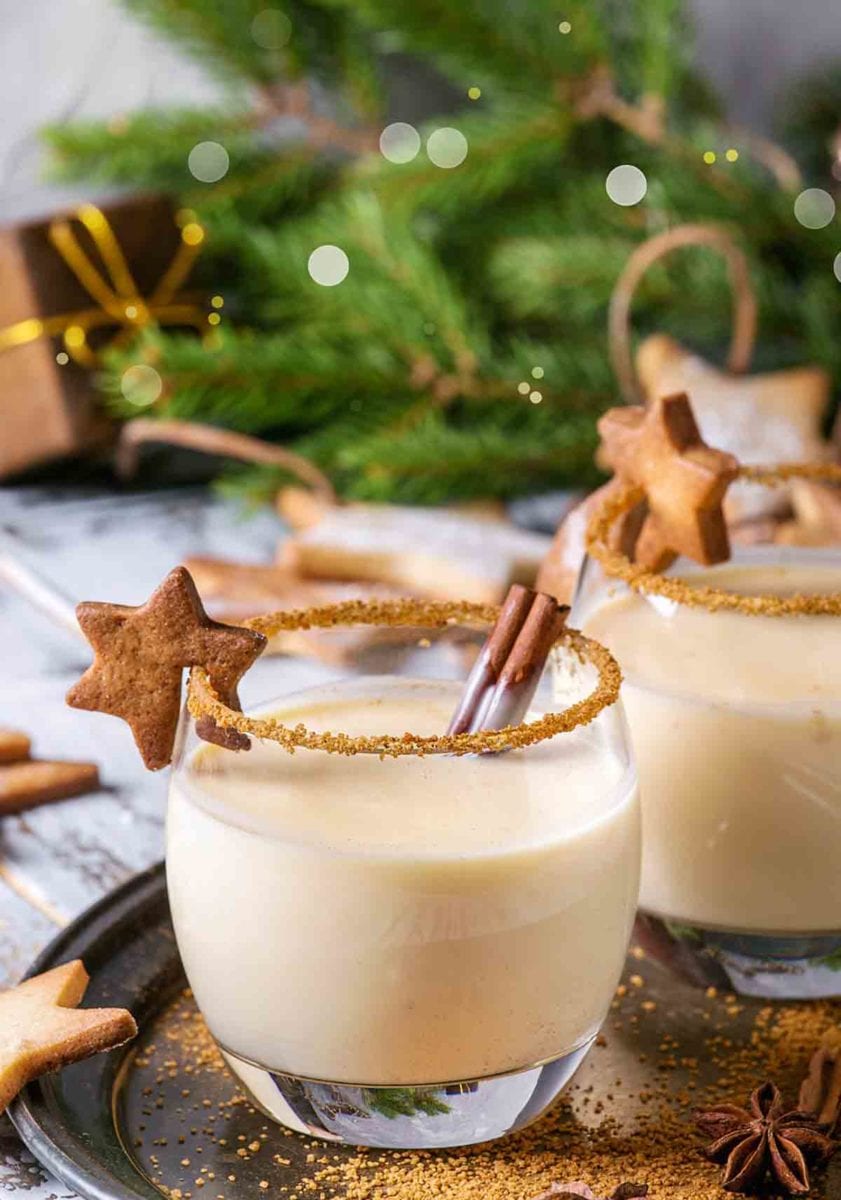 TTwo eggnogs in glasses with a gingerbread star on the lip and a rim of cinnamon.
