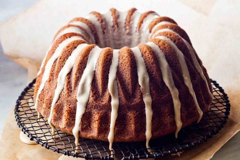 An espresso cake drizzled with glaze on a wire rack that is set on a pice of parchment to catch any glaze drips.