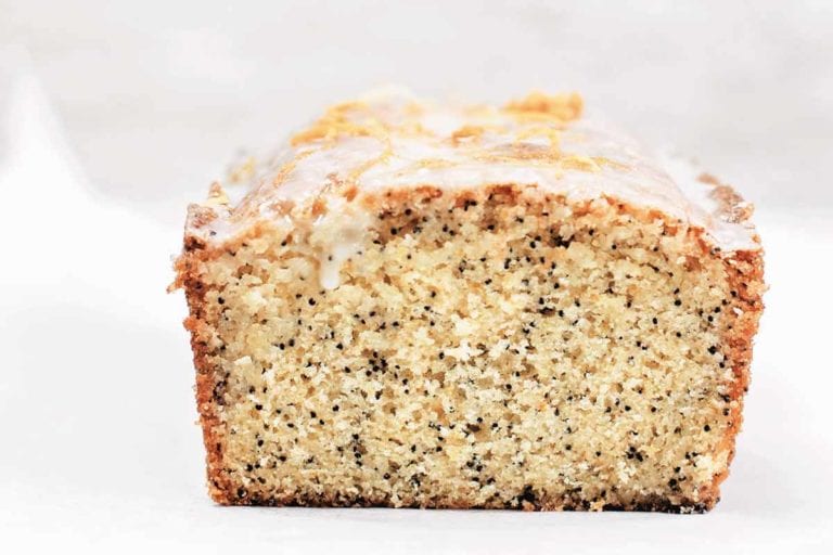 A cut loaf of lemon-poppy seed cake on a white background
