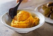 A ceramic bowl filled with pumpkin ginger mash with a person scooping a spoon into it.