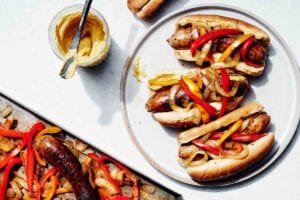 Three sheet pan sausage, peppers, and onions on a white plate with a jar of mustard beside it.