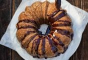 A spiced sweet potato bundt cake on a piece of parchment, being drizzled with chocolate glaze.