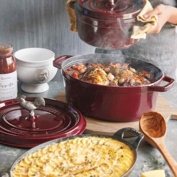 Staub Coq Au Vin Cocotte in use shown in maroon with scalloped potatoes on side.