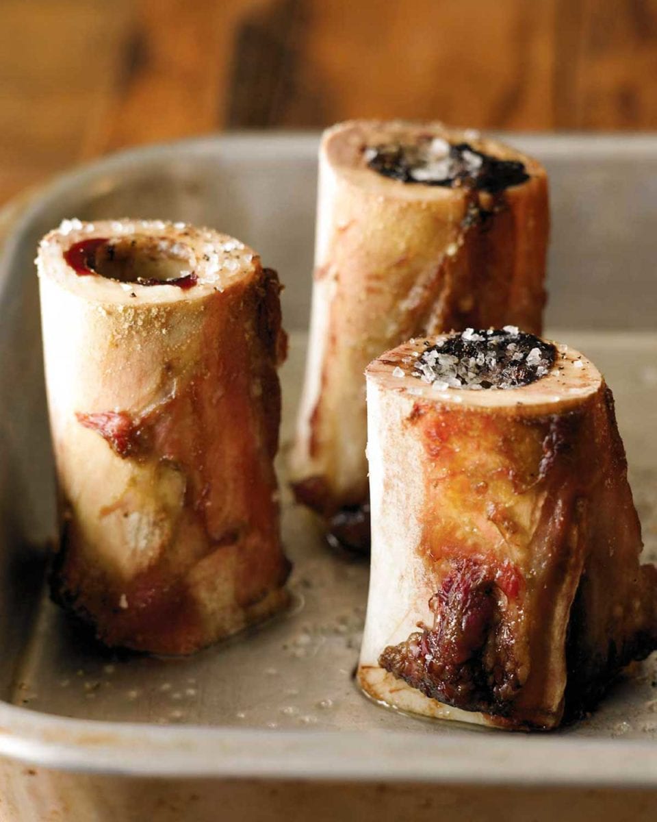 Three pieces of roasted bone marrow sprinkled with salt in a metal roasting pan.