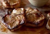 Four juicy seared maple-brined pork chops with pear chutney on a cutting board